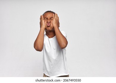 Funny African American boy fooling around making grimaces, patting puffy cheeks, keeping eyes closed, wearing casual clothes, isolated on white. Carefree, happy childhood. Kids and lifestyle