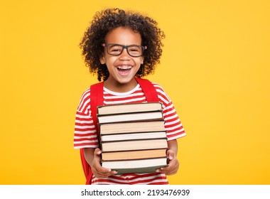Funny african american boy in glasses hugging books and laughing at camera while studying at school against yellow background - Shutterstock ID 2193476939