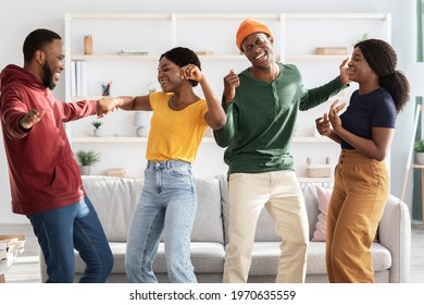 Funny african american friends dancing and singing at home, positive black men and women standing in the middle of living room, moving and laughing, enjoying weekend together