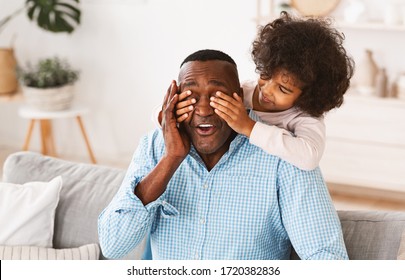 Funny African American girl closing her granddad's eyes from behind, surprising him or playing guess who game - Shutterstock ID 1720382836