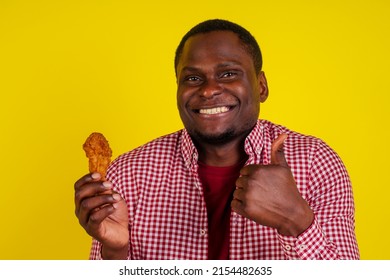 funny african american man eating fried chicken leg in studio yellow background