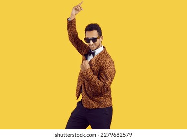 Funny African American man wearing a leopard party suit, bowtie and trendy sunglasses dancing in the studio. Portrait of a happy young black guy dancing isolated on a yellow colour background - Shutterstock ID 2279682579
