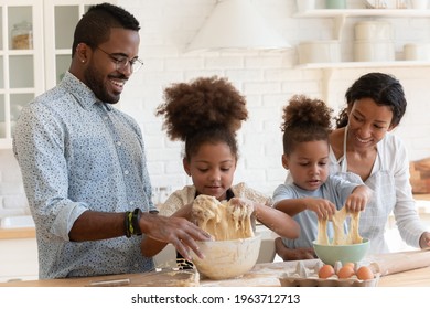 Funny African American Parents Helping Cute Kids To Knead Dough, Enjoying Kitchen Activities. Happy Family With Children Baking Dessert For Dinner Together. Couple Teaching Son And Daughter To Cook