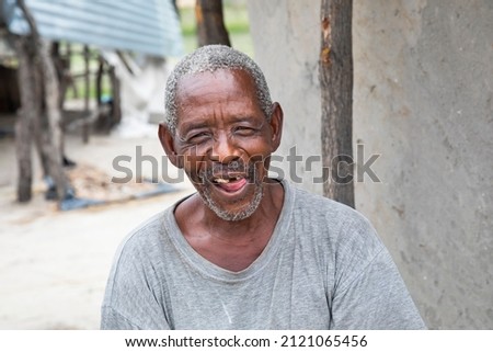funny African old man smiling in the yard of his house in a village in Botswana, 