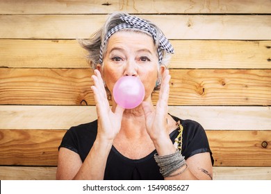 Funny and alternative old people caucasian beautiful woman with pink bubble chewing gum - portrait of youth active senior lady having fun - no limit age lifestyle concept