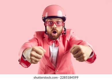 Funny amazed astonished excited open mouthed ginger bearded man in pink helmet, funky suit, bow tie holds pretend steering wheel, drives modern rent car, panics, races ahead forward in adrenaline rush
