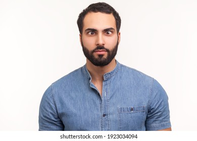 Funny amused man with beard in blue shirt crossing his eyes looking crazy and stupid, fooling around, having fun, vision problems. Indoor studio shot isolated on white background