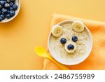 Funny animal face on baby porridge in a bowl. Top view, yellow background, colorful, breakfast.