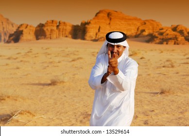 Funny arabic man playing terrorist by point and shoot with his hands in Wadi Rum desert at sunset, Jordan