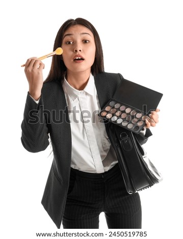 Funny Asian businesswoman with briefcase applying makeup on white background
