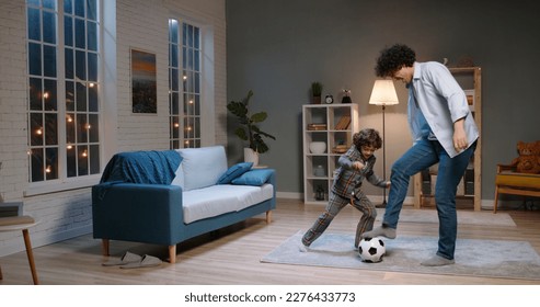 Funny asian father and kid with curly hair are playing football together at home. Young man dribbling ball while son tries to take it - happy family, togetherness concept  - Powered by Shutterstock