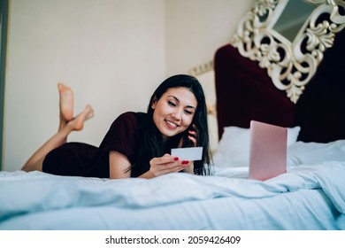 Funny Asian Female Freelancer With Laptop Computer Checking Mobile Contact On Business Card While Dialing Number And Calling, Cheerful Woman Phoning Via Cellphone Technology Talking And Smiling