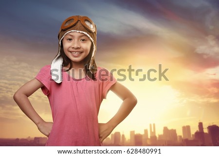 Funny asian kid with aviator hat dreaming of becoming a pilot against sunset at sky