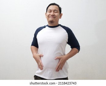 Funny Asian man closing eyes and smiling while holding his distended belly, fully satisfied expression after eating delicious food concept - Shutterstock ID 2118423743
