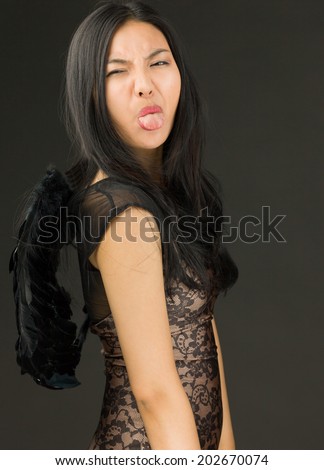 Funny Asian young woman dressed up as a black angel sticking out her tongue