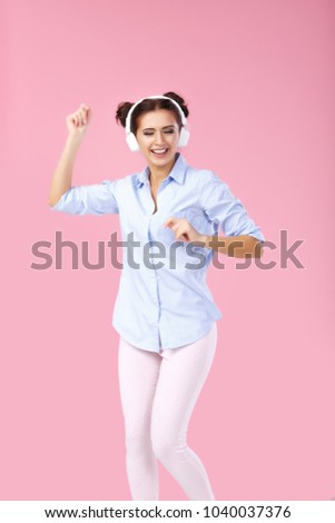 funny attractive woman in headphones listening to music and dancing on pink background