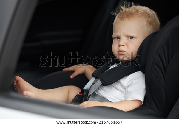 Funny baby boy in a car seat. Thoughtful\
child sits in the car. Passenger safety\
concept