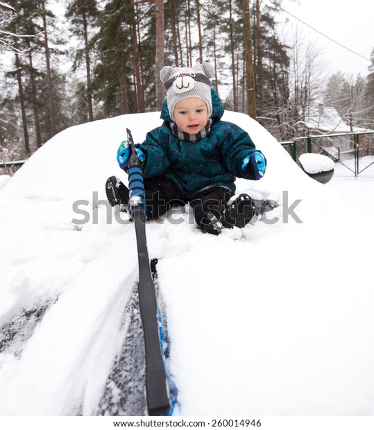 Funny baby boy\
cleans car bonnet from\
snow
