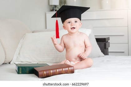 Funny baby boy in diapers wearing black graduation cap