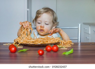 Funny Baby Child Getting Messy Eating Spaghetti With Tomato Sauce From A Large Plate, By Itself With His Hands, At Home