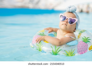 Funny baby girl on summer vacation. Child having fun in swimming pool. Sweet toddler swimming in a floating ring in a pool. Water park. Holidays.
