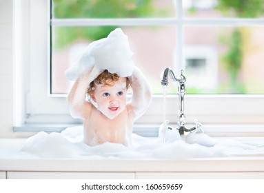 Funny baby girl playing with water and foam in a big kitchen sink