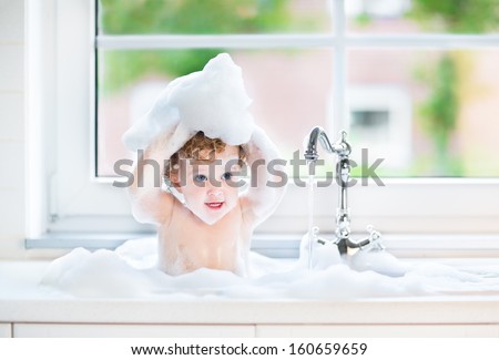 Funny baby girl playing with water and foam in a big kitchen sink