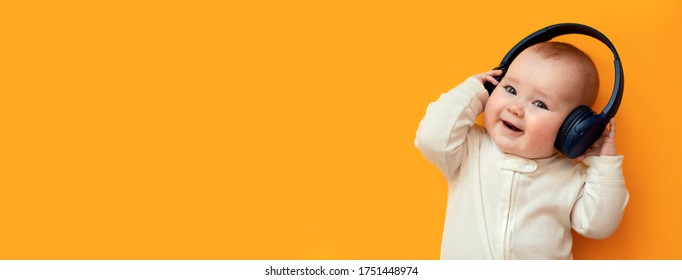 Funny baby with headphones listening to music on the orange background. Banner with empty space.