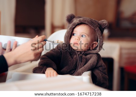 Funny Baby Sitting in Highchair Refusing to Eat. Small infant being a picky eater disliking the food
