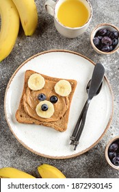 Funny Bear Face Sandwich From Buckwheat Bread With Peanut Butter, Banana, Frozen Blueberries And Orange Juice. Healthy Children's Breakfast.