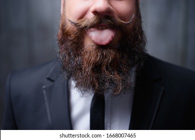 Funny beard and moustache. Close-up of young bearded man showing tongue.