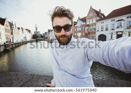 Funny bearded hipster taking selfie portrait in Bruges old town, Belgium. Handsome male blogger takes photo for social media.