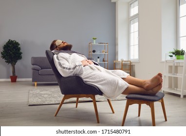 Funny Bearded Man In A Bathrobe In A Sleep Mask Lies In A Comfortable Chair In The Living Room.