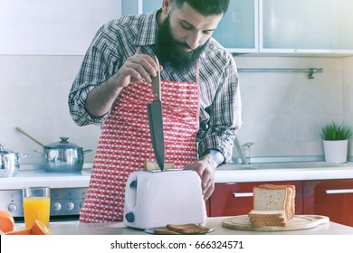 funny bearded man at kitchen making toasts for breakfast and repairing toaster with knife
