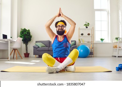 Funny Bearded Man Wearing Headband And Glasses Sitting In Easy, Cross-legged Yoga Pose On Exercise Mat With Arms Raised, Doing Breathing Hatha Exercise And Learning To Meditate During Weekend At Home