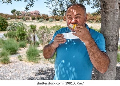 Funny Bearded Middle Aged Man Eating Vegan Sandwich On The Street Under Shadow Of The Tree. Unhealthy Eating. Fast Food. Takeaway Food