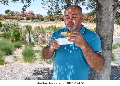 Funny Bearded Middle Aged Man Eating Vegan Sandwich On The Street Under Shadow Of The Tree. Unhealthy Eating. Fast Food. Takeaway Food