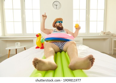 Funny bearded overweight man in beachwear and sunglasses lying on bed and water mattress with cocktail and imagining himself on beach on vacation. Funny male look concepts