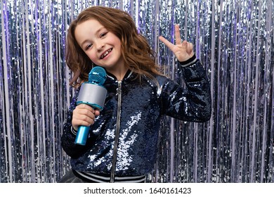 Funny Beautiful Holiday Host Holds A Microphone In Her Hands And Shows The Class Against A Background Of Shiny Tinsel