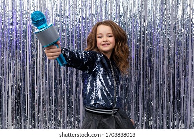 Funny Beautiful Holiday Host Holds The Microphone Up On A Background Of Shiny Tinsel