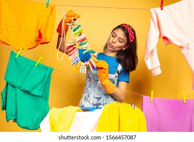 Funny and beautiful housewife doing housework isolated on yellow background. Young caucasian woman surrounded by washed clothes. Domestic life, bright artwork, housekeeping concept. Folding the - Shutterstock ID 1566457087
