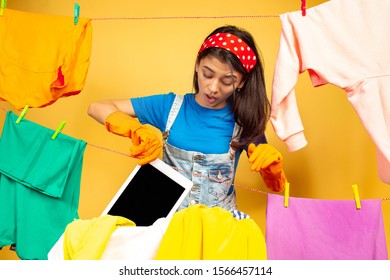 Funny and beautiful housewife doing housework isolated on yellow background. Young caucasian woman surrounded by washed clothes. Domestic life, bright artwork, housekeeping concept. Has washed tablet. - Shutterstock ID 1566457114