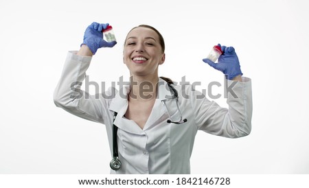 Funny beautiful smiling doctor in medical uniform, rubber gloves dancing with packs of different pills in her hands, having fun and fooling around, isolated white background. Joyful happy nurse