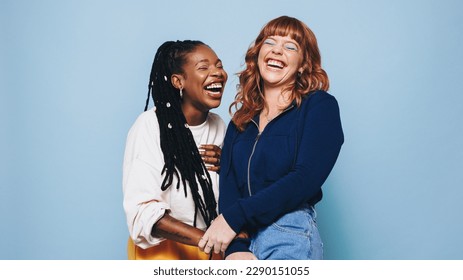 Funny best friends laughing cheerfully while standing together in a studio. Two happy young women enjoying themselves against a purple background. Female friends making memories together. - Powered by Shutterstock