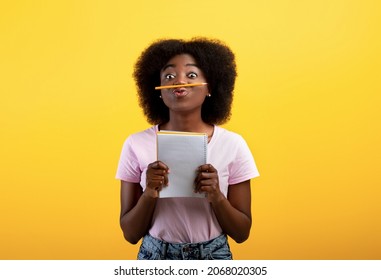 Funny black female student keeping pencil between nose and lips as moustach and holding notebook, posing over yellow studio background, copy space - Powered by Shutterstock