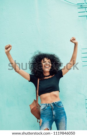 Lustige schwarze Frau mit Afrohaar, die die Arme im Freien hebt.