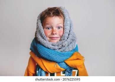 Funny blond freckled kid boy portrait. Smiling child playing while put on many scarves in the winter cold weather. School boy in warm hat and scarf on a white background. Sick or not. - Powered by Shutterstock