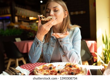 Funny blonde girl in jeans jacket eating pizza at restaurant. - Shutterstock ID 1390308734