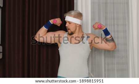 Funny bodybuilder sportsman guy couch showing biceps. Stylish hipster man blogger trainer recording sport fitness online boxing exercises with dumbbells vlog at home. Joke, comical meme, parody, humor