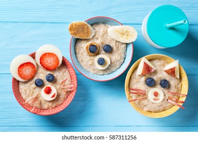 Funny bowls with oat porridge with cat, dog and mouse faces made of fruits and berries, food for kids idea, top view